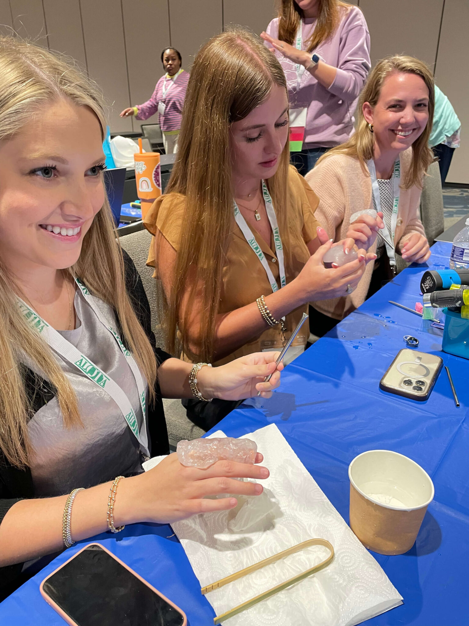 Three women sit at a table engaged in a hands-on AT fabrication activity with craft supplies, smiling and focused