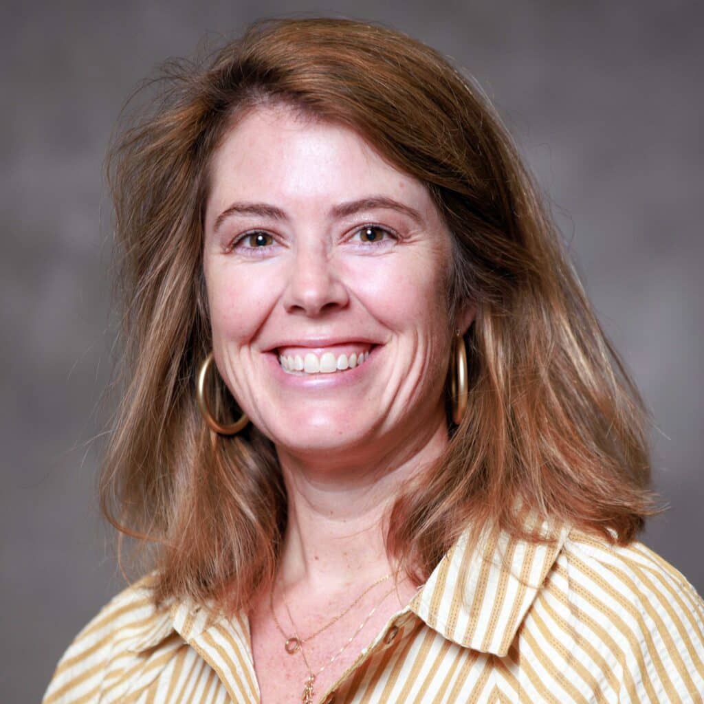 Elizabeth Stewart has shoulder-length light brown hair, wearing a beige and white striped shirt and gold hoop earrings.