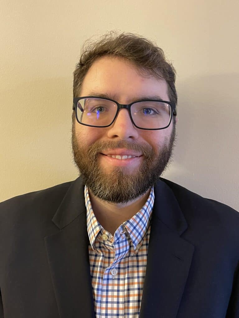 Steven Inman has glasses, a beard, and short brown hair, wearing a dark blazer over a checkered shirt.