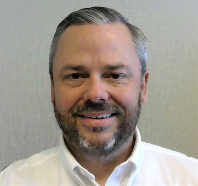 Nick Nyberg has short gray hair and a trimmed beard, smiling at the camera, wearing a white collared shirt.