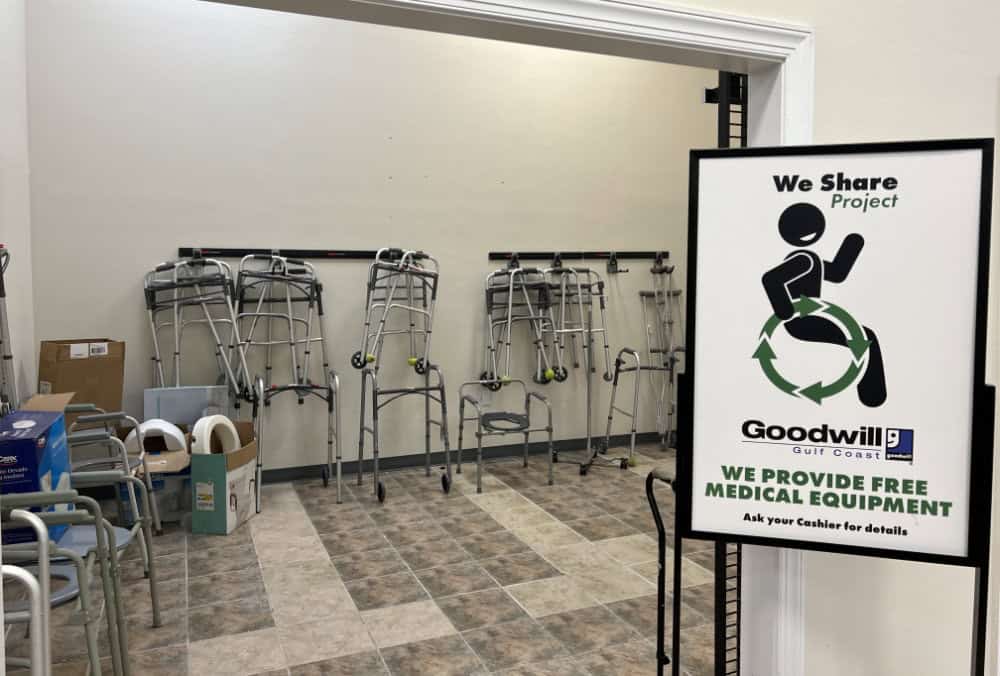 Room with several walkers and mobility aids against the wall, and a sign stating "We provide free medical equipment" from Goodwill Gulf Coast We Share Project.