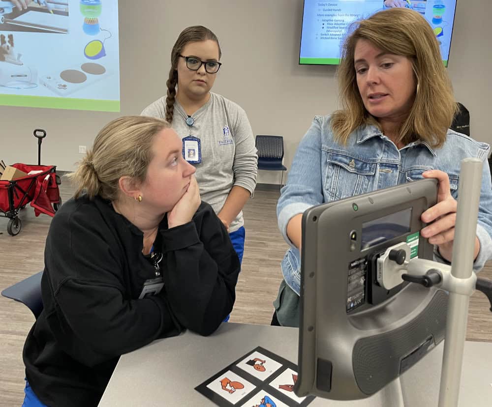 Elizabeth from APTAT shows 2 women how to use a communication device placed on a table